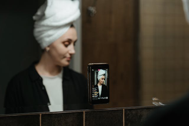 バスルームの鏡の前でスキンケアをしながら、Instagram ライブセッションをする女性。