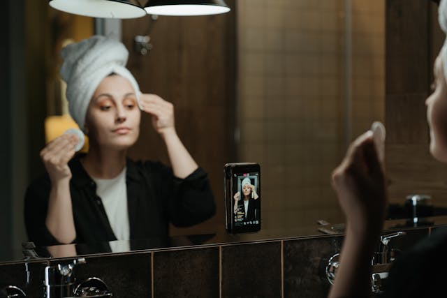 O femeie care își face rutina de îngrijire a tenului în fața oglinzii în timp ce înregistrează pe Instagram Live.