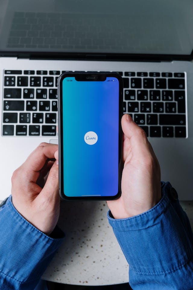 Una persona che tiene in mano un telefono con il logo di Canva su uno sfondo blu.