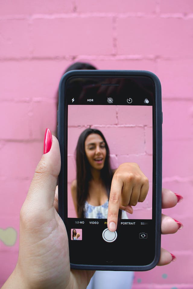 Iemand neemt een foto van een vrouw met haar telefoon terwijl ze haar hand uit het camerascherm steekt en op de opnameknop tikt.