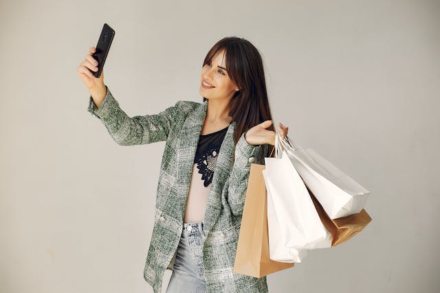 A woman holding plenty of shopping bags smiling while taking a selfie.