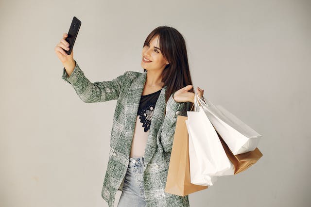 Une femme tenant de nombreux sacs de courses sourit en prenant un selfie.