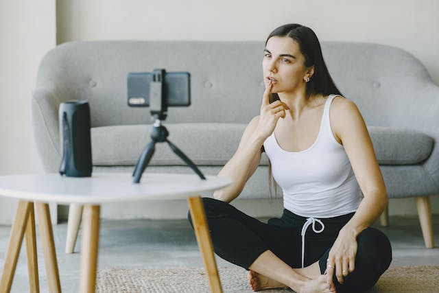 A woman thinking while recording herself in front of a smartphone.