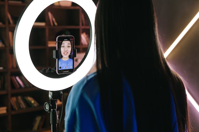 A young female influencer recording a video of herself talking to her followers with her phone and ring light.