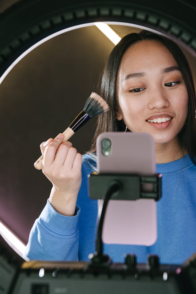 ビューティコンテンツのクリエイターが、化粧ブラシを宣伝するために携帯電話と三脚を使って撮影している。