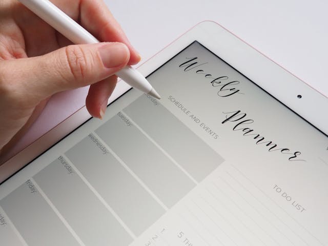 Jemand hält einen Stift in der Hand, um Notizen in ein Kalenderblatt auf einem Tablet zu schreiben.