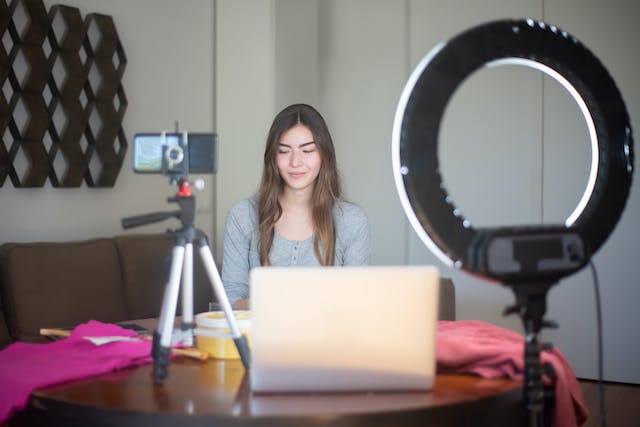 A female influencer creating content using her phone, tripod, ring light, and laptop.
