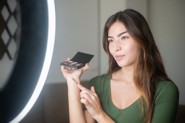 A female influencer holding up a makeup palette while filming a product review video.
