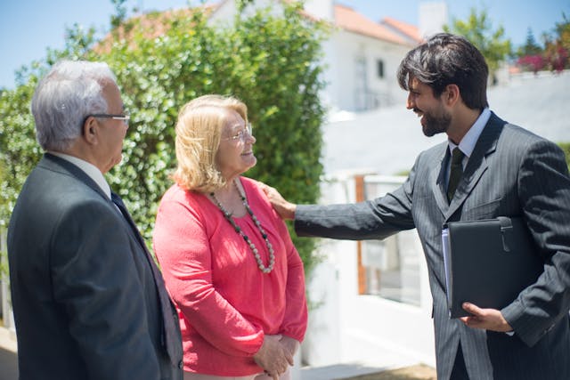 Een man in een grijs pak lacht naar een vrouw in een roze jurk. 