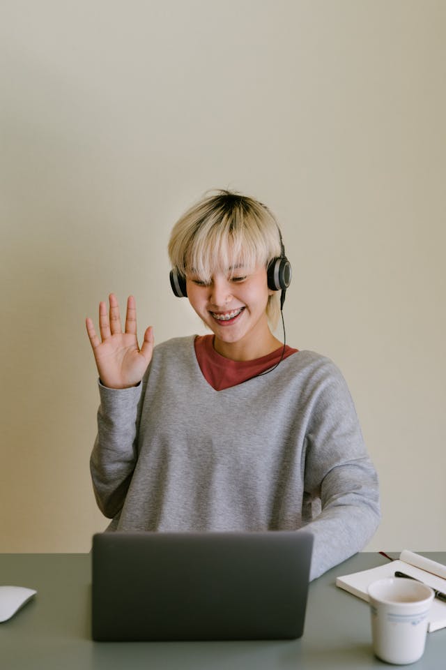 Een vrouw tijdens een videogesprek op haar laptop die gedag zwaait naar iemand met wie ze een verbinding heeft.