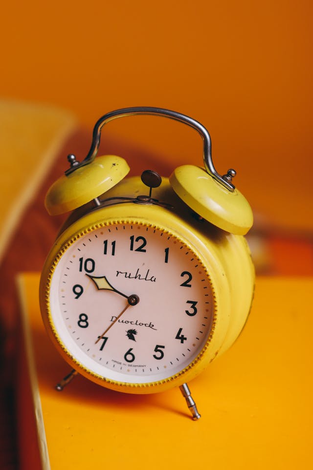 Um despertador vintage branco e amarelo sobre uma mesa amarela.