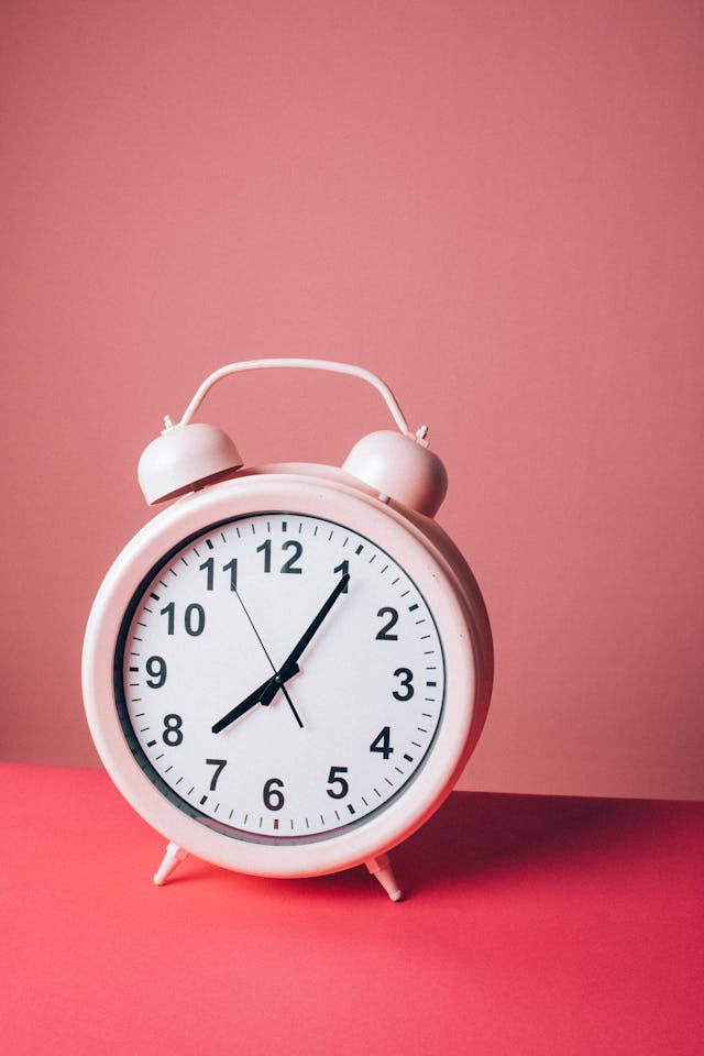 A pink and white alarm clock on a hot pink surface.