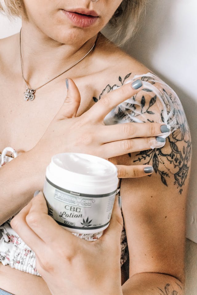 Une femme appliquant une lotion sur son épaule tatouée.