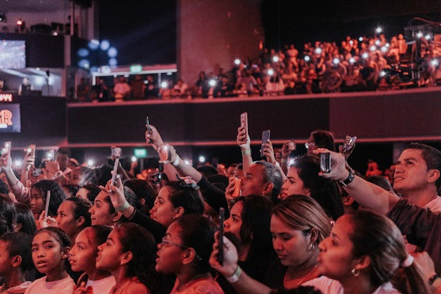 A crowded stadium audience taking photos of an on-stage performer with their phones.