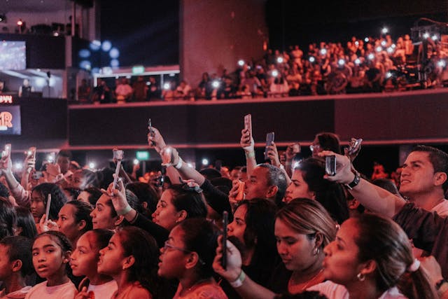 Um público de um estádio cheio a tirar fotografias de um artista em palco com os seus telemóveis.