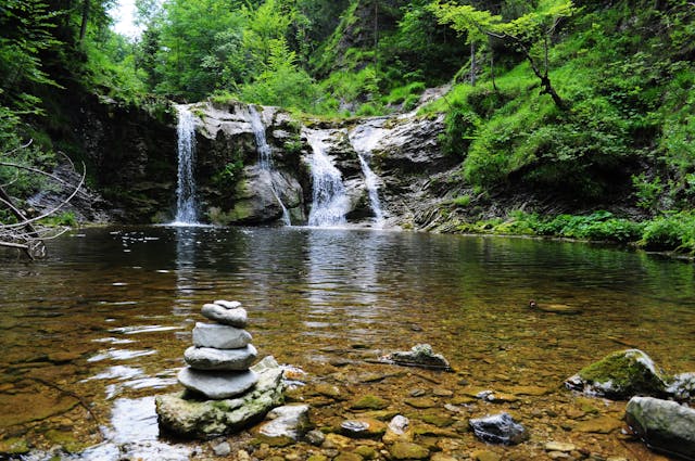 Uma vista desimpedida de uma cascata com rochas e vegetação em redor.