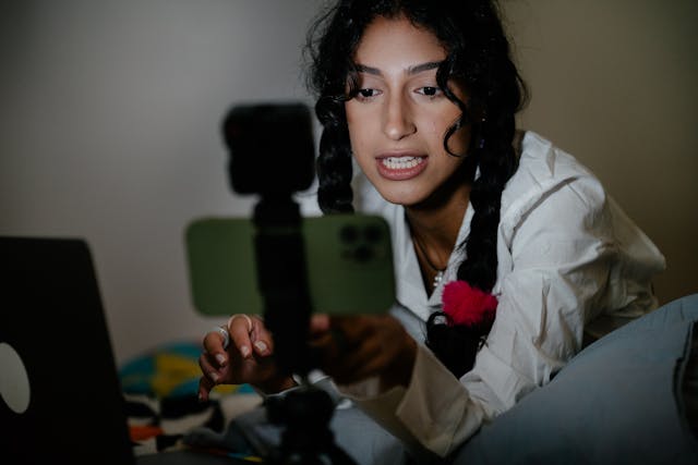 A woman in a dark room sets up her phone on a tripod.