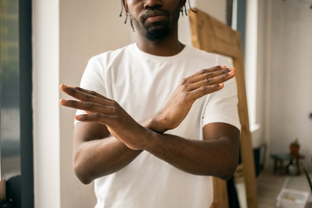 Een man in een wit shirt toont een gebaar van een stopteken met gekruiste handen.