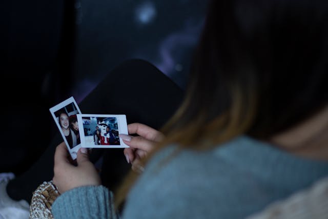 A woman holding two Polaroid photos and looking at them.