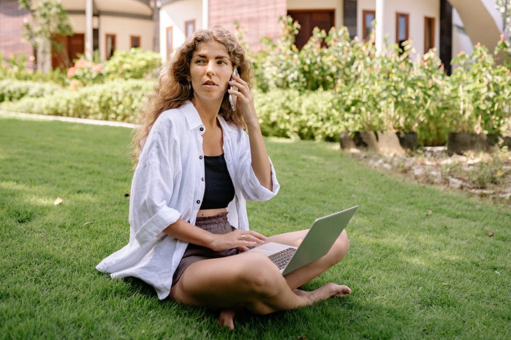 A woman making a call while using a laptop.