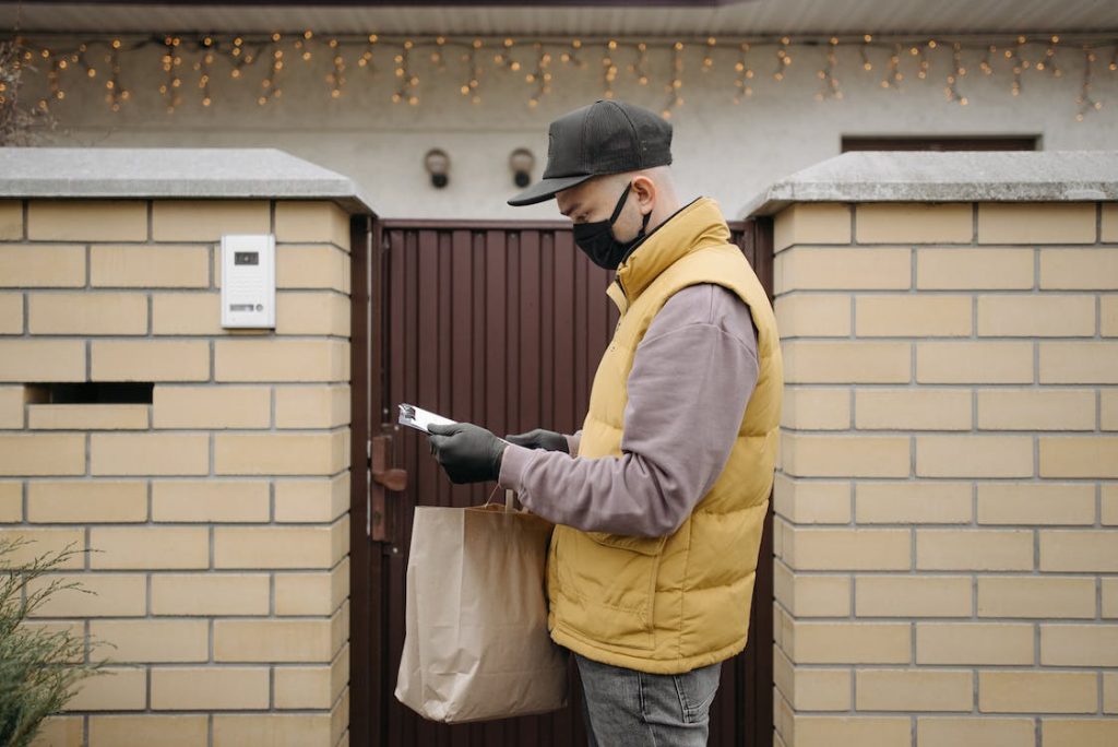 Un hombre sostiene una bolsa mientras consulta su teléfono delante de un portal.