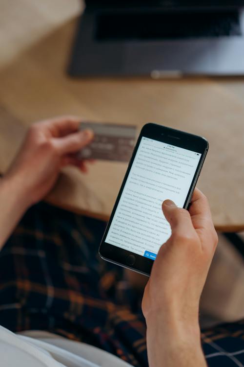 A person using his phone while holding a card.