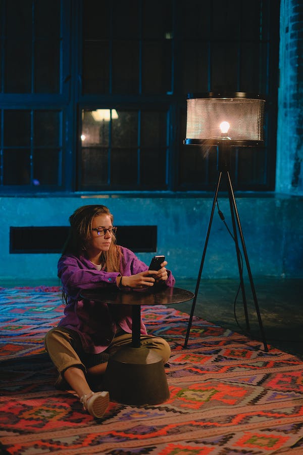 A woman sits on the floor while she scrolls her phone.