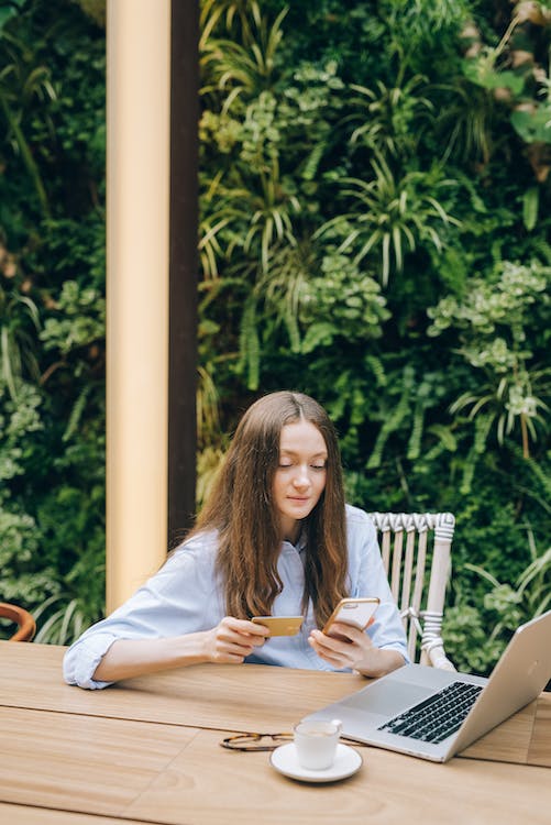 A woman curiously thinking while holding a card and looking at her laptop.