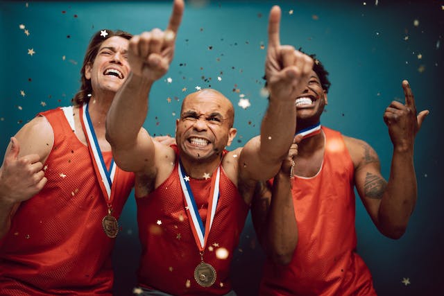 Three happy male athletes wearing gold medals with confetti around them.