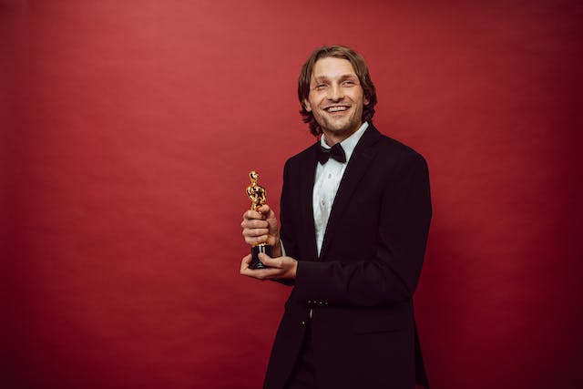 A man wearing a tuxedo smiling while holding a trophy.