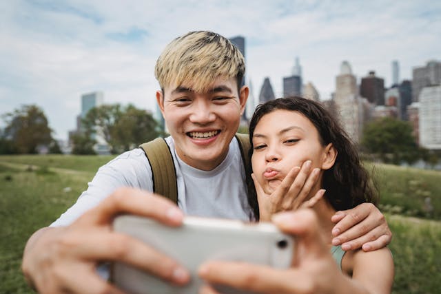 A man and woman laughing and making funny faces while taking selfies.