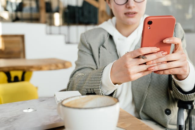 A woman scrolling through her phone while holding a pen.