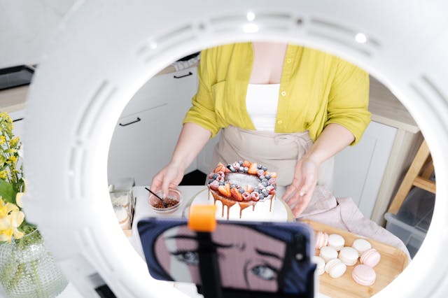 A woman filming a video of herself baking a cake using a camera phone, tripod, and ring light.