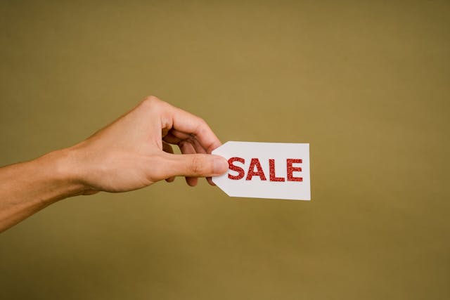 Someone holding a card that says “SALE” in bold, red letters.