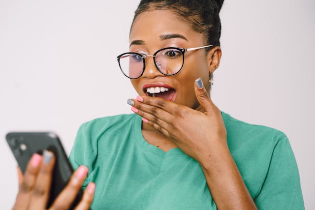 Una donna che si copre la bocca e fa una faccia scioccata mentre guarda qualcosa sul suo telefono.