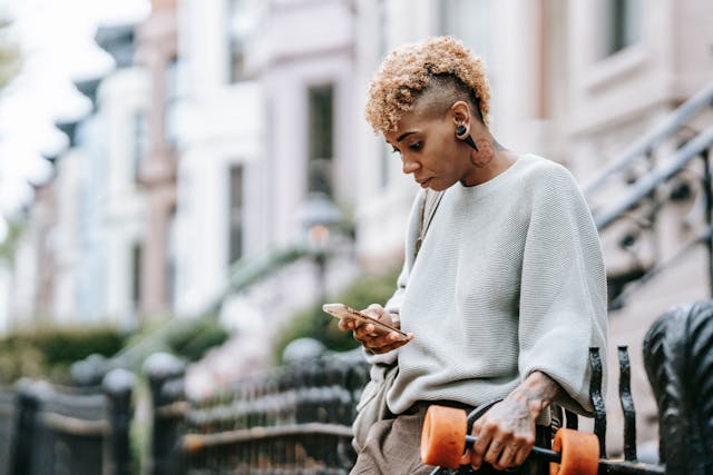 A woman scrolling her phone while holding a skateboard on the other side.
