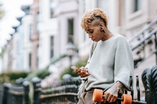 Une femme fait défiler son téléphone tout en tenant un skateboard de l'autre côté.