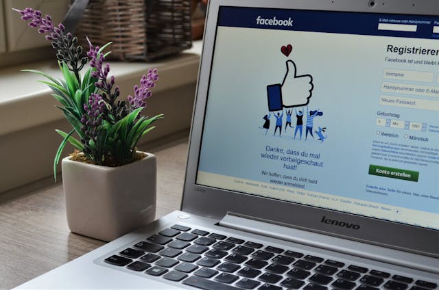 テーブルの上に置かれたノートパソコンにフェイスブックのログイン画面が表示され、その横に植物が置かれている。