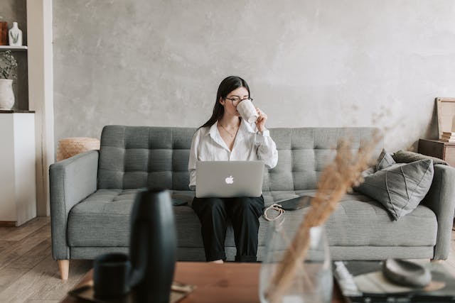 Una donna seduta su un divano che sorseggia un caffè mentre lavora al suo computer portatile.