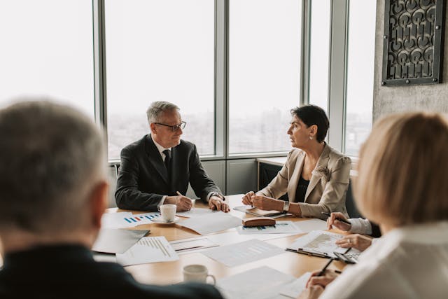 A group of people are engaged in a business meeting with papers spread around them. 