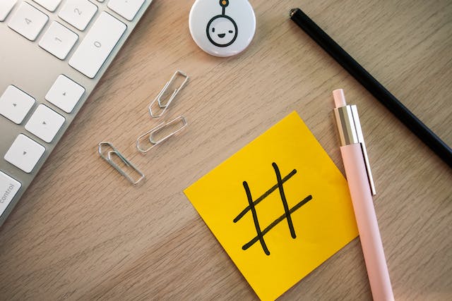 Des fournitures de bureau sur un bureau avec une note jaune autocollante portant le symbole du hashtag.