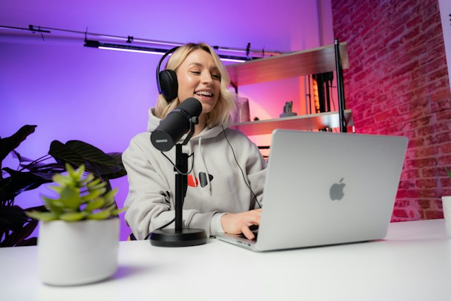 Uma rapariga sorri em frente ao seu computador portátil com um microfone ao lado.