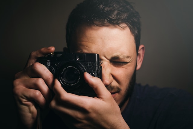 Nahaufnahme eines Mannes, der mit einer Kamera vor einem schwarzen Hintergrund ein Foto macht.
