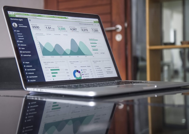 A laptop with analytics displayed is placed on a glass-top table. 