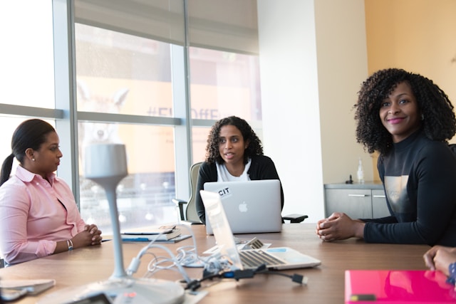 Three women are sitting and talking in a corporate setting. 