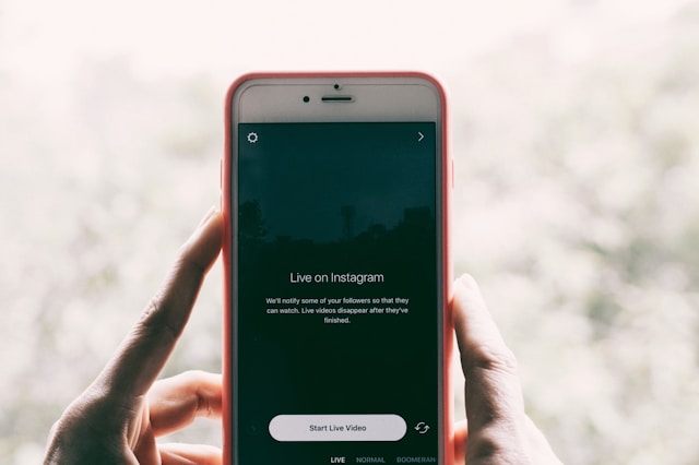 Instagram ライブ画面とスタートボタンが表示された携帯電話を持つ人。
