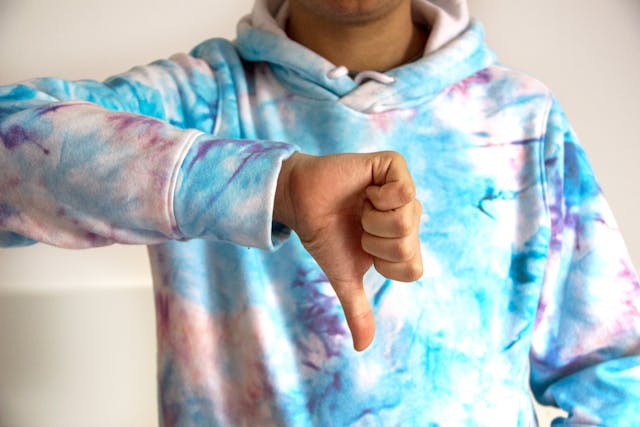 Someone in a tie-dye hoodie making a thumbs-down motion.