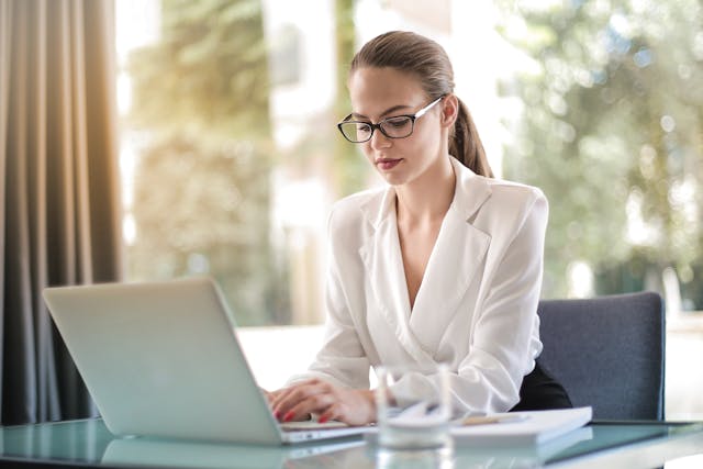  Mulher de negócios de aspeto profissional, com óculos, a escrever no seu computador portátil.