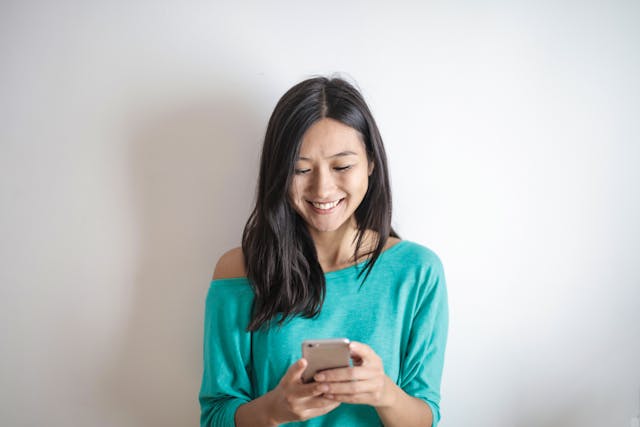 Een vrouw glimlacht terwijl ze naar haar telefoon kijkt om iets te lezen.