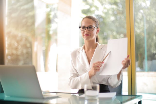 A businesswoman holding a report and pointing to it with a pen.